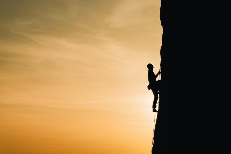 A person climbing a steep mountain representing self-growth through challenges.