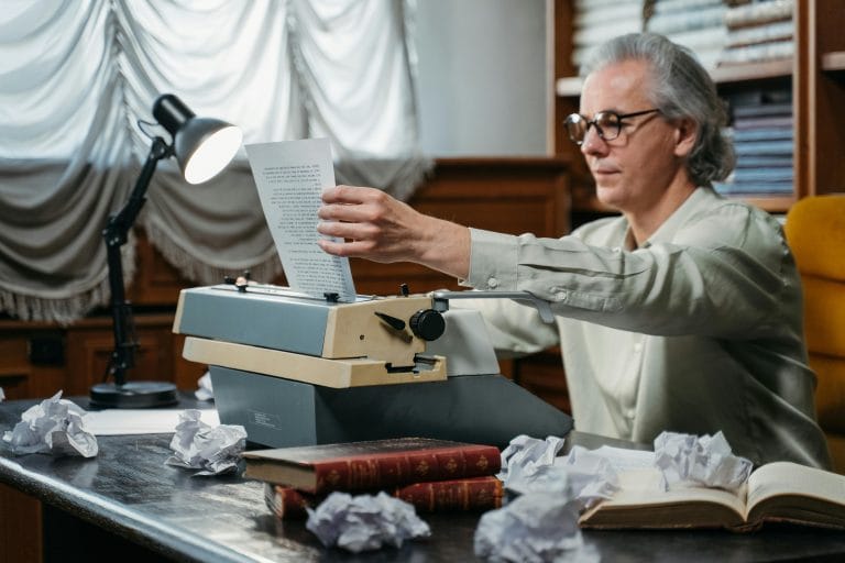 Writer with books, illustrating ambition’s impact on literature and society.