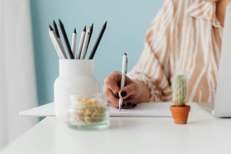 A journal with a pen on a desk surrounded by calming green plants.