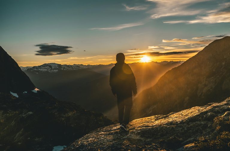 Person standing on a mountain peak at sunrise, symbolizing overcoming challenges.