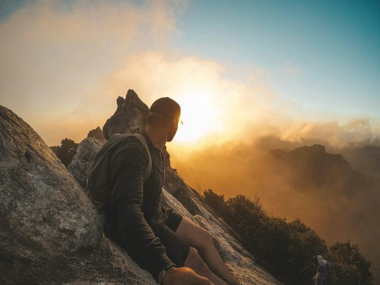 Person on mountain peak looking at sunrise, representing a unique life-changing opportunity